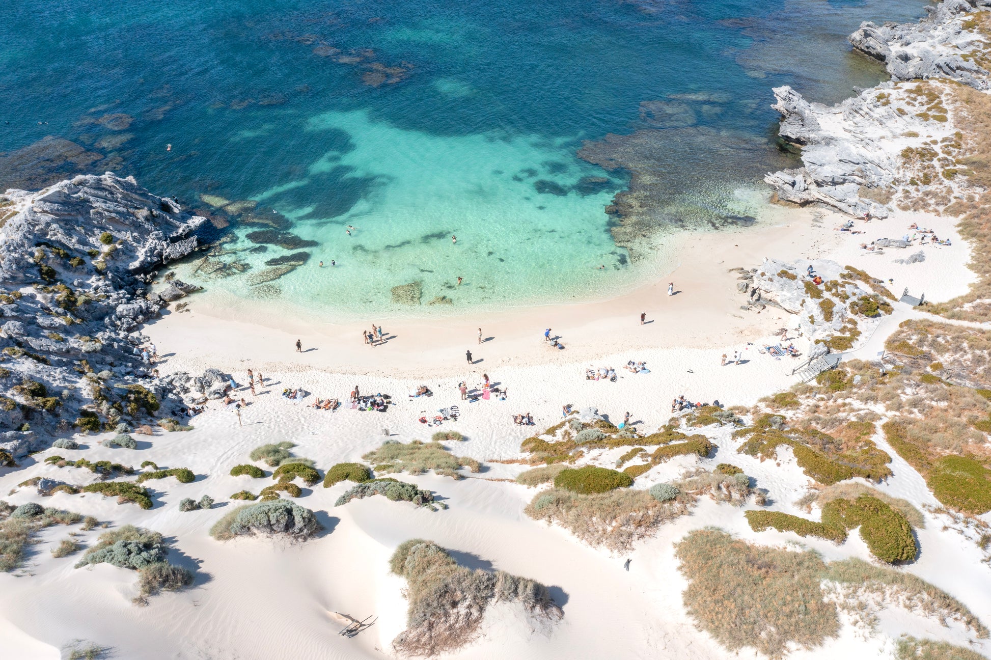 Beach scene with people enjoying the water and sand, surrounded by greenery.