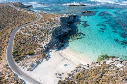 Aerial view of a coastal landscape with a winding road, rocky cliffs, and clear blue water.