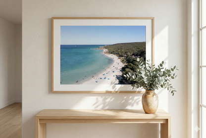 Framed beach photograph on a wall above a wooden console table with a plant.