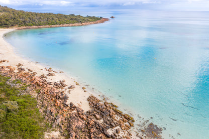 Coastal scene with clear blue water, rocky shore, and greenery.