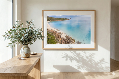 Framed beachscape on a wall with a wooden desk and plant in the foreground