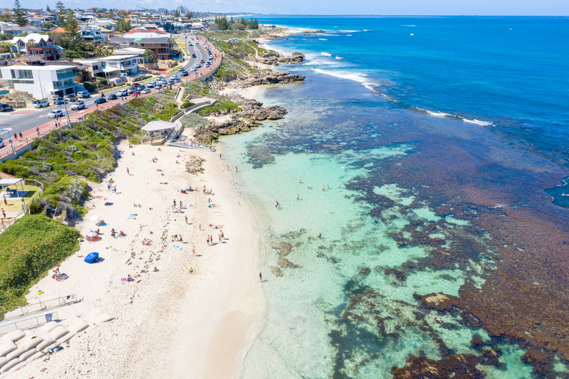 Beach scene with clear blue water and a coastal road.