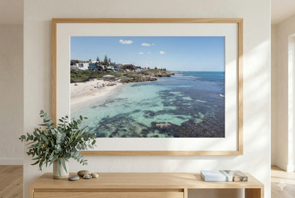 Framed photograph of a coastal scene on a wall above a wooden console table with decorative items.