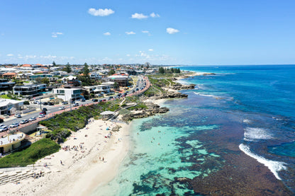 Coastal town with houses, beach, and clear blue water under a bright sky.