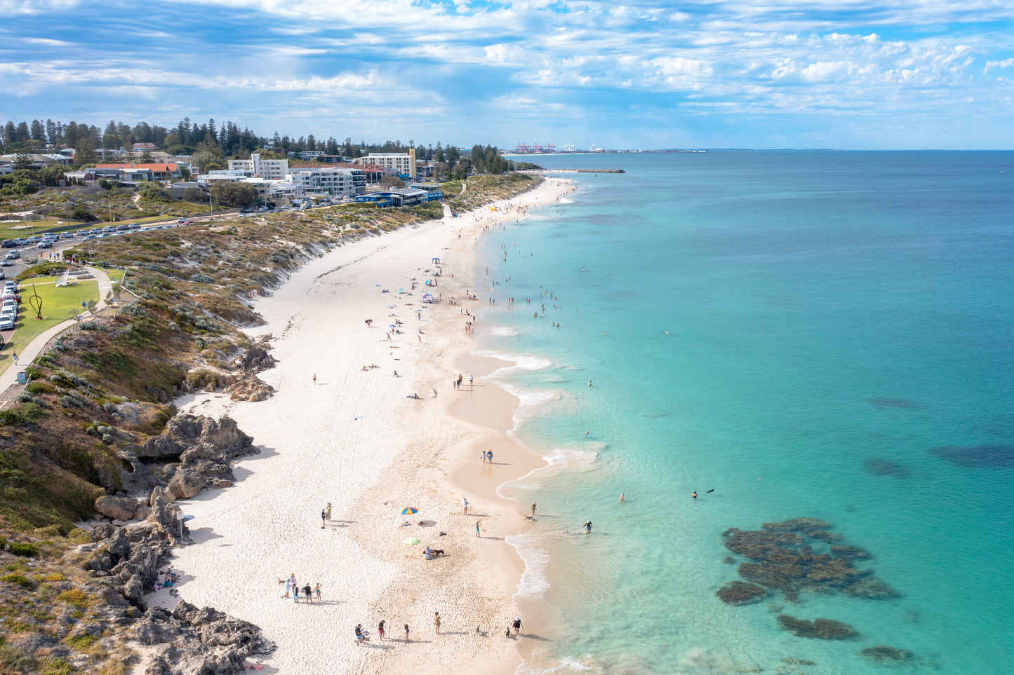 Aerial view of a beach with clear blue water and a coastal town in the distance.