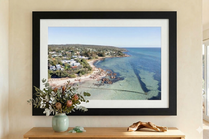 Framed artwork of a coastal scene on a wall with a vase and decorative item below.