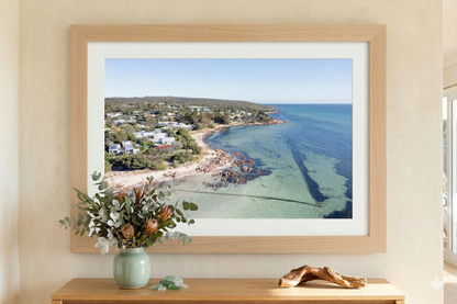 Framed photograph of a coastal scene on a wall above a wooden console table with a vase and driftwood.