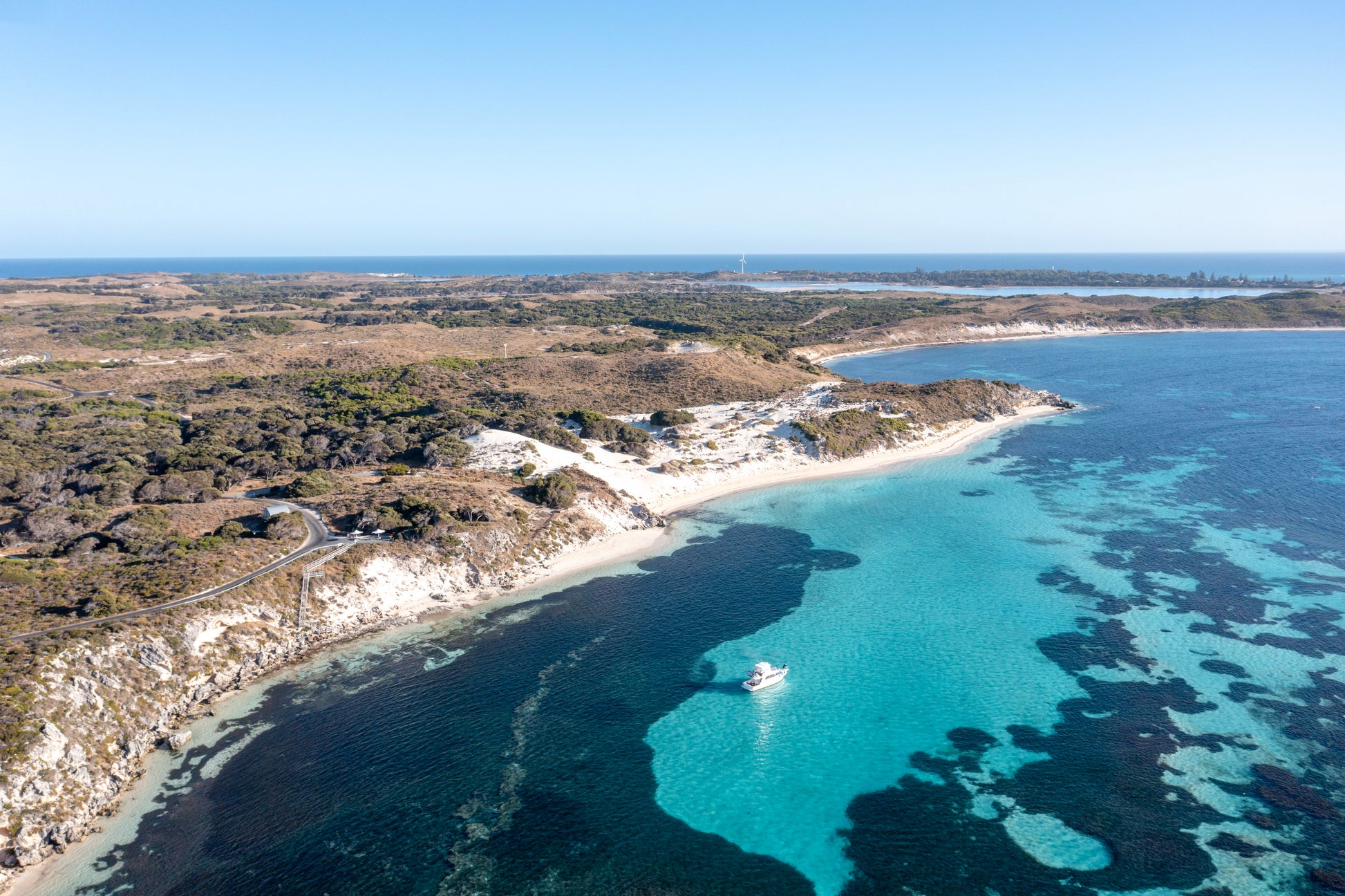 Aerial view of a coastal landscape with clear blue water and a white boat.