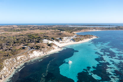 Aerial view of a coastal landscape with clear blue water and a white boat.
