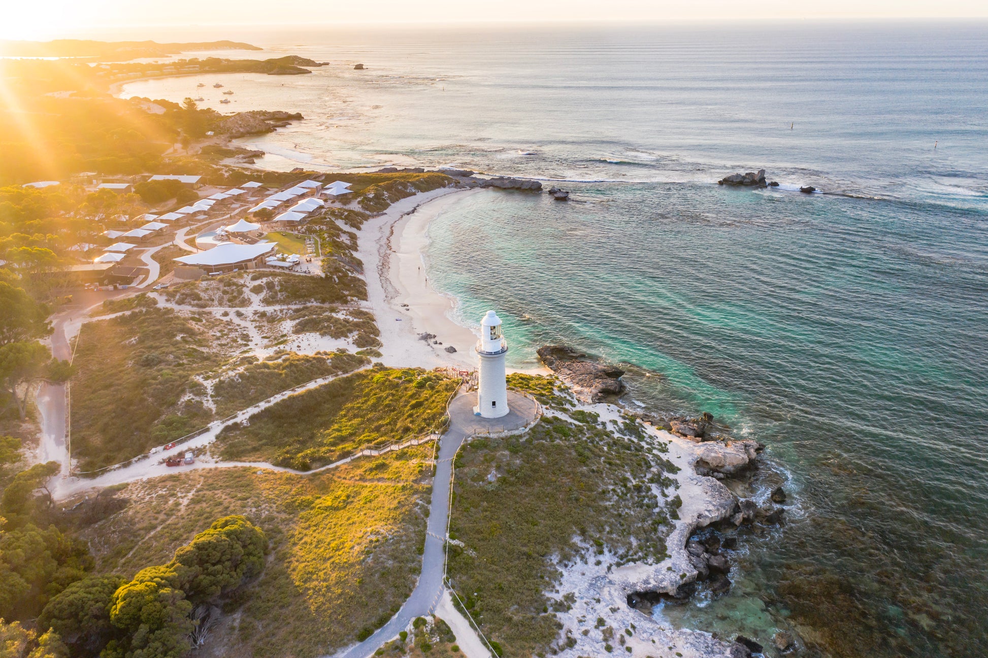 Lighthouse on a rocky island with a clear sky and sun.