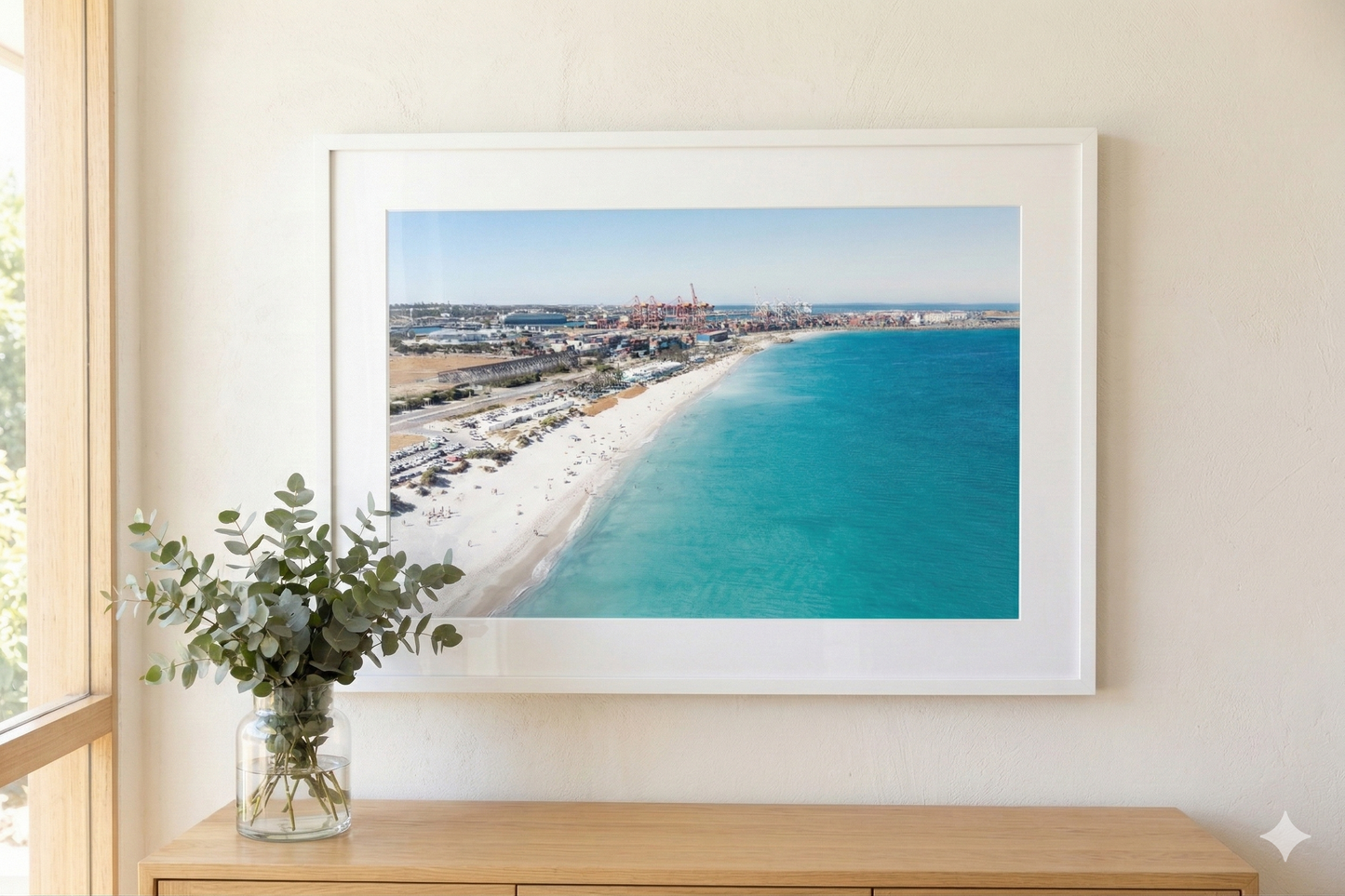 Framed artwork of a beach scene on a wall above a wooden console table with a plant.