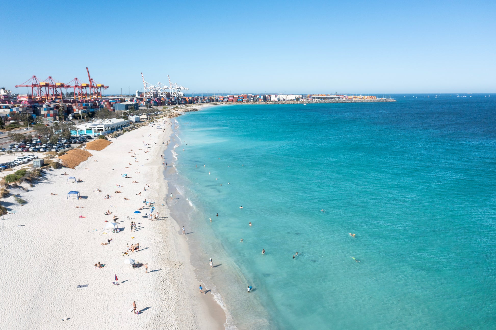 Beach scene with clear blue water and a distant port.