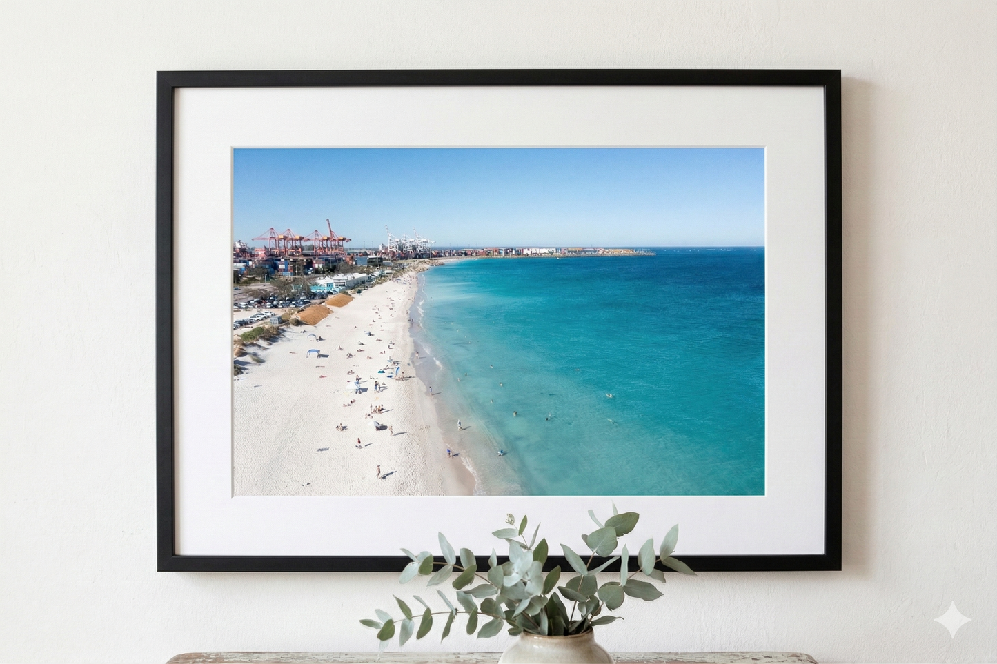 Framed photograph of a beach scene with clear blue water and white sand, displayed on a wall.