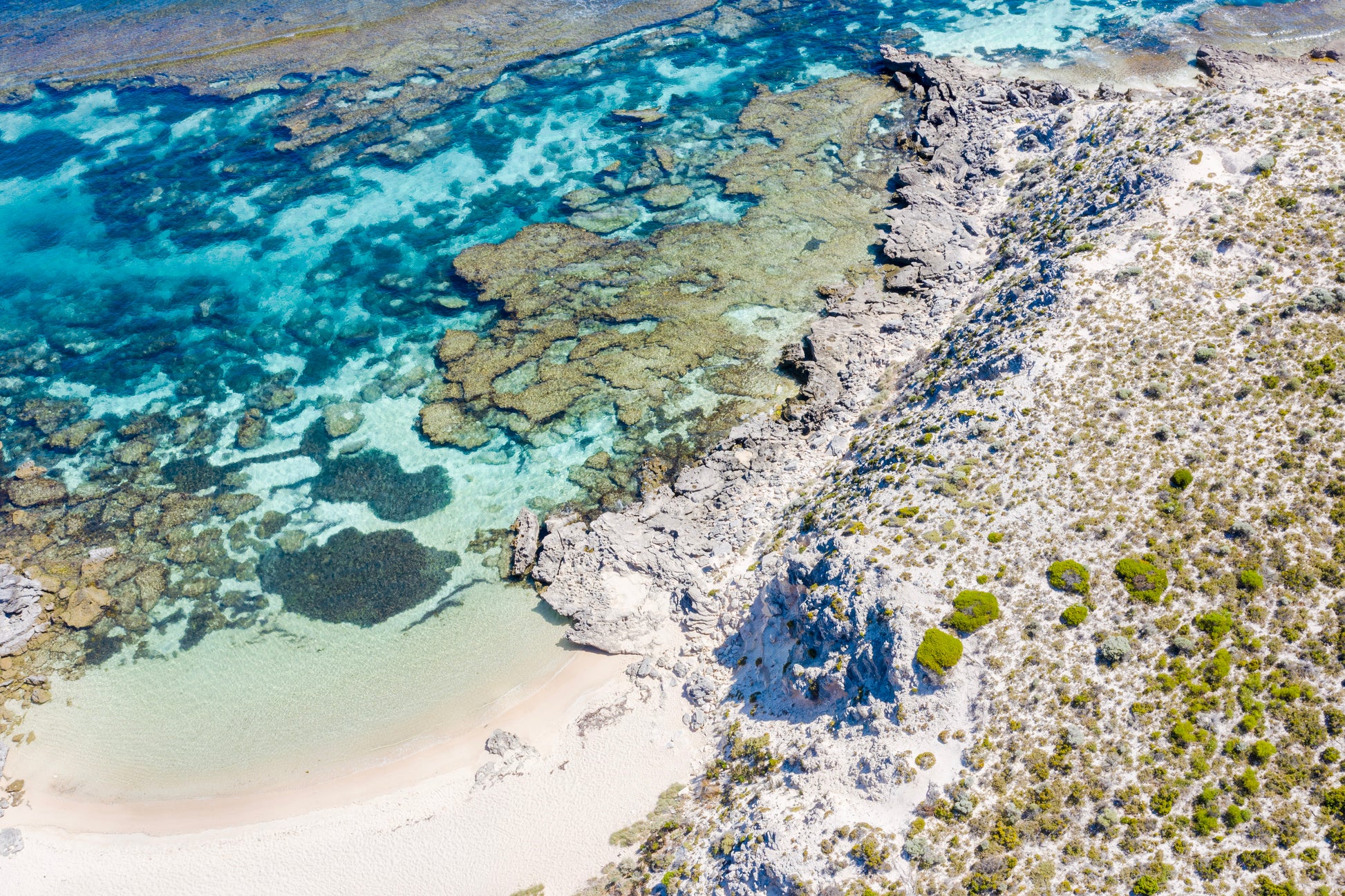Aerial view of a coastal landscape with clear blue water, white sand, and rocky outcrops.