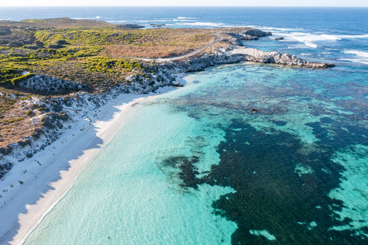 Aerial view of a beach with clear turquoise water and rocky shoreline.
