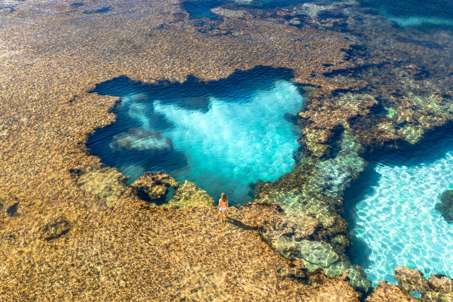 Person standing on a rocky outcrop with clear blue water below, The Basin ,Rottnest Island Western Australia