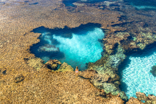 Person standing on a rocky outcrop with clear blue water below, The Basin ,Rottnest Island Western Australia