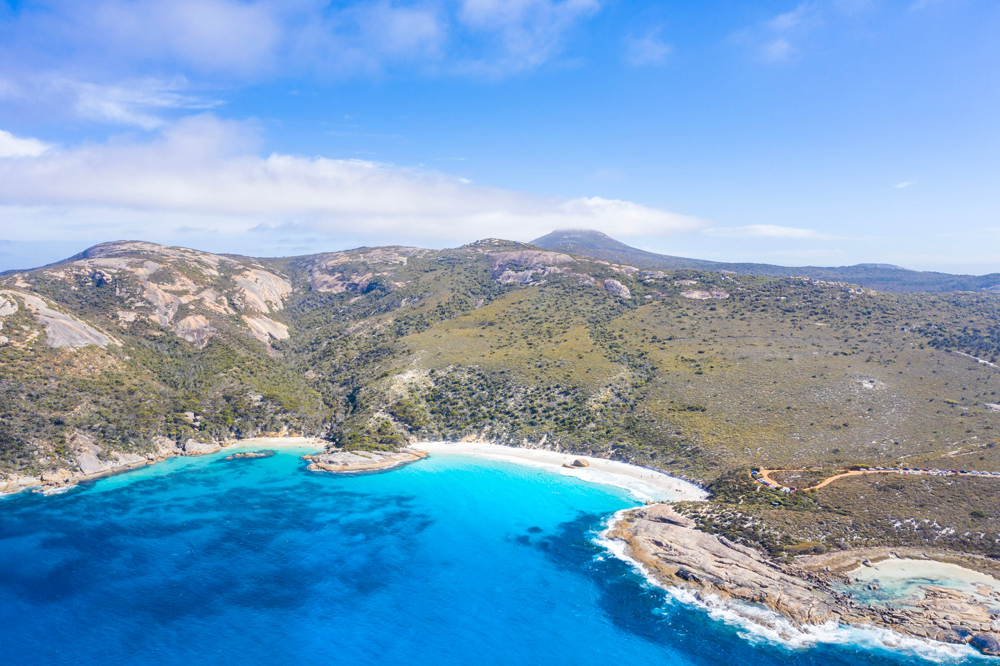 Aerial view of a coastal landscape with clear blue water and green hills under a blue sky.