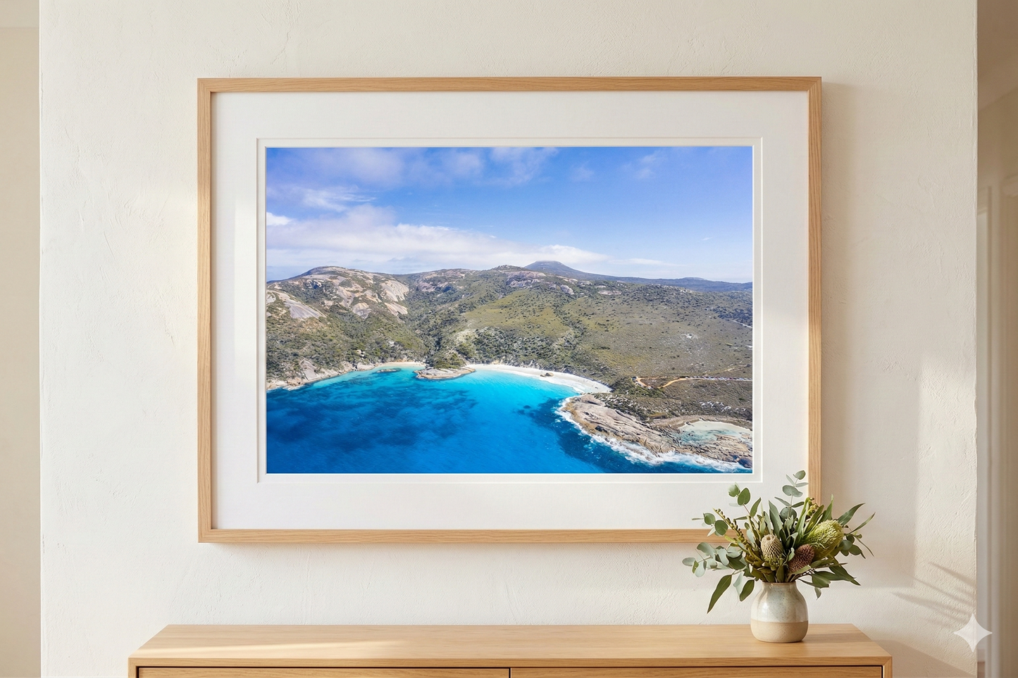 Framed photograph of a coastal landscape with blue water and green hills on a white wall.