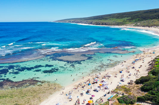 A fine art print of a beach scene with clear blue water, greenery, and people enjoying the sun and surf.