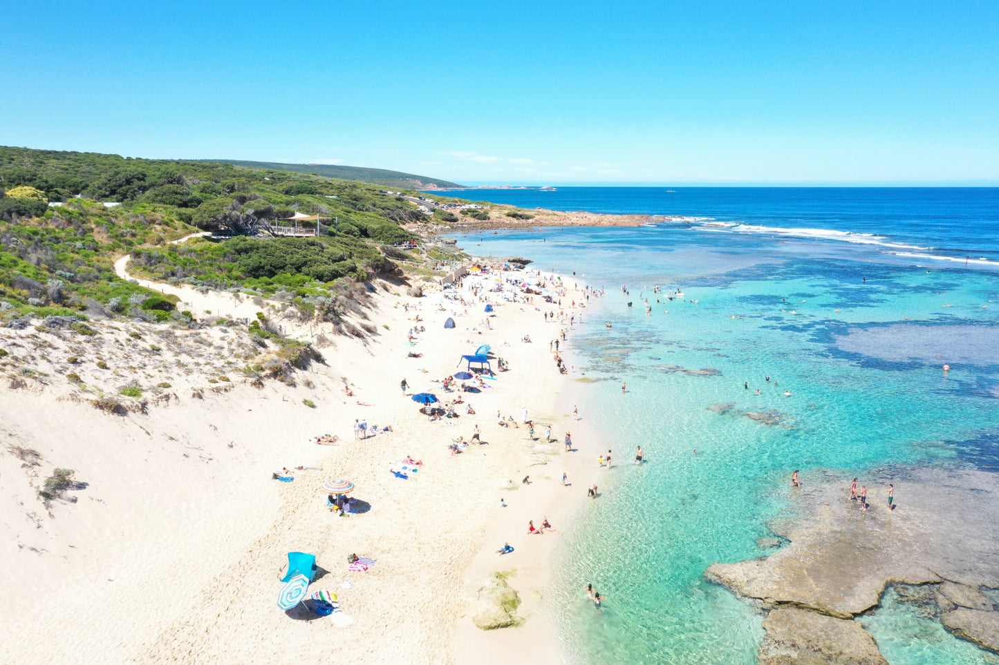 Beach scene with clear blue water and white sand, people enjoying the sun.