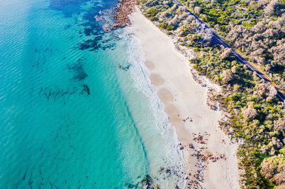 A scenic view of Eagle Bay with clear blue water, white sandy beach, and greenery in the background, captured from above.