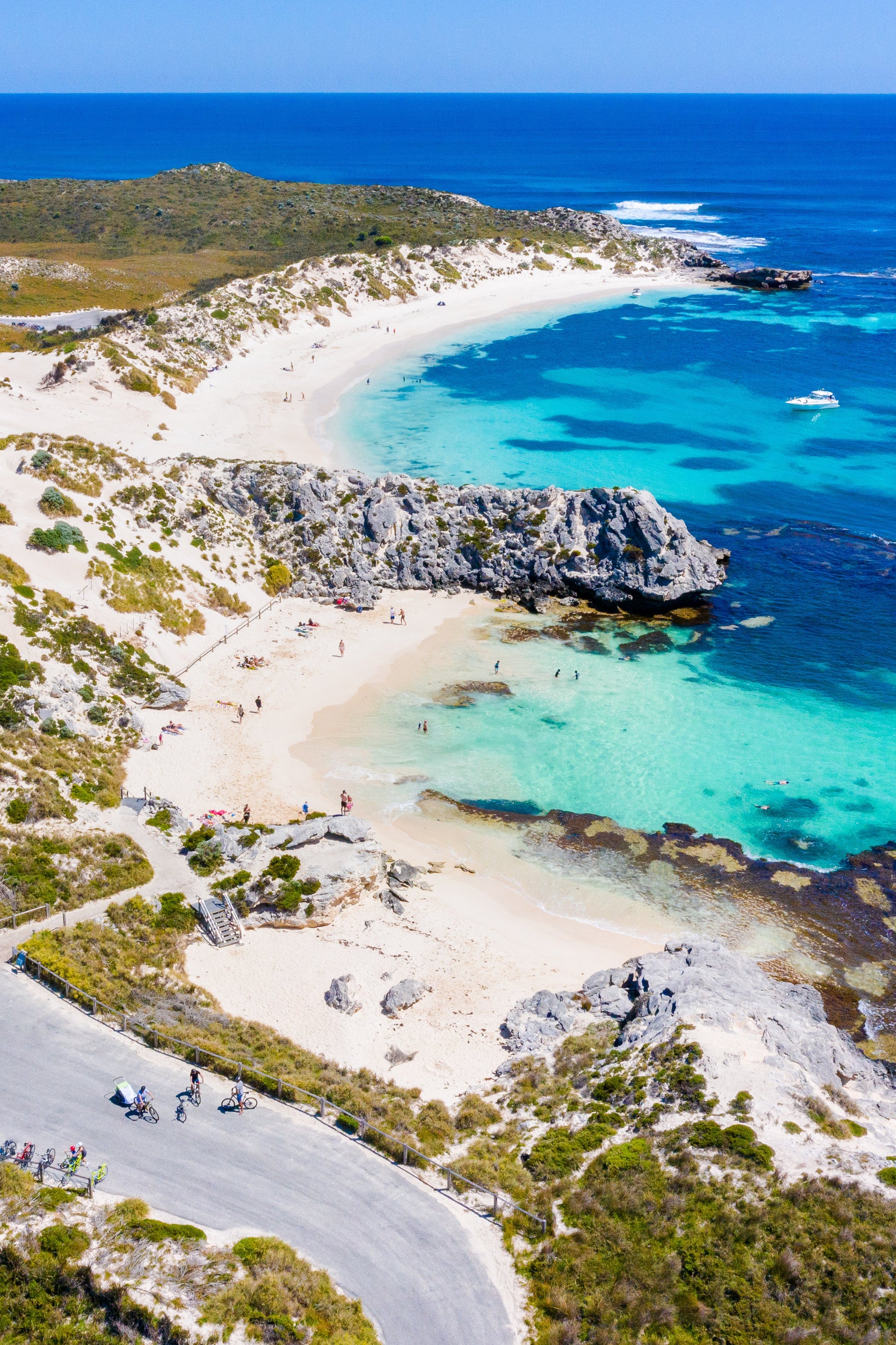 A scenic view of a beach with clear blue water and rocky cliffs, possibly part of Rottnest Island.