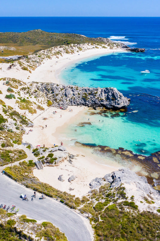 A scenic view of a beach with clear blue water and rocky cliffs, possibly part of Rottnest Island.