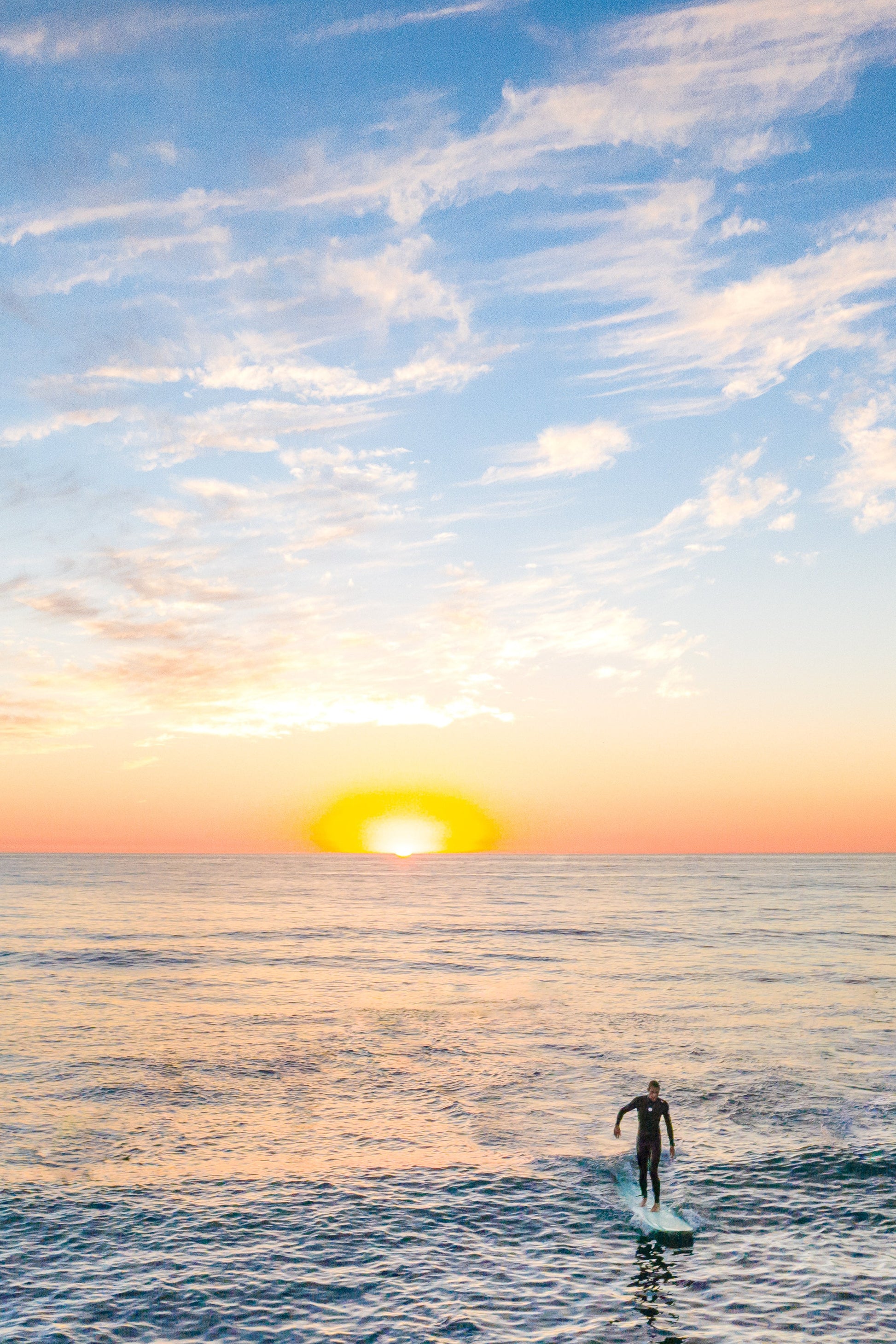A fine art print featuring a sunset over the ocean with a silhouette of a person surfing.