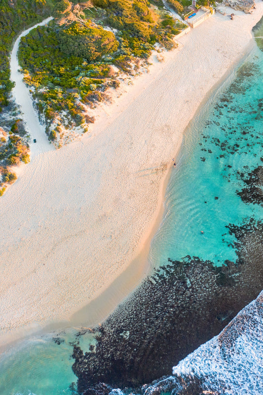 A fine art print featuring a coastal landscape with a sandy beach, clear water, and greenery in the background.